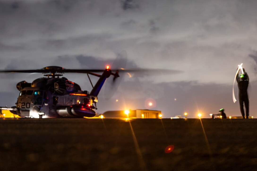 A large helicopter sits on a lit tarmac at night.