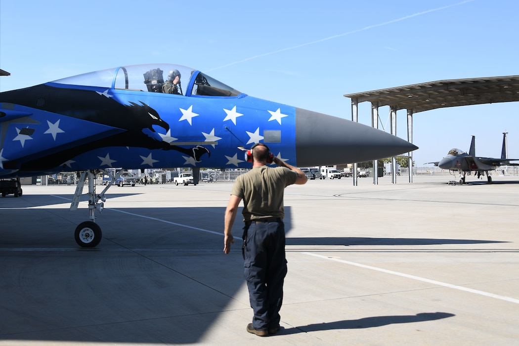 U.S. Air National Guard Staff Sgt. Paul Rojeski, 144th Aircraft Maintenance Squadron crew chief, marshals out  an F-15C Eagle that recently reached 10,000 flight hours Oct. 21, 2022, at the Fresno Air National Guard Base, Calif. To celebrate the achievement, members of the 144th Maintenance Squadron structural shop painted the aircraft with an American flag scheme. (U.S. Air National Guard photo by Staff Sgt. Mercedes Taylor)