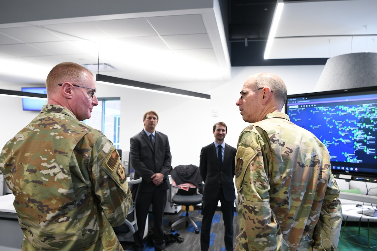 Photo shows group standing around big monitor speaking to one another