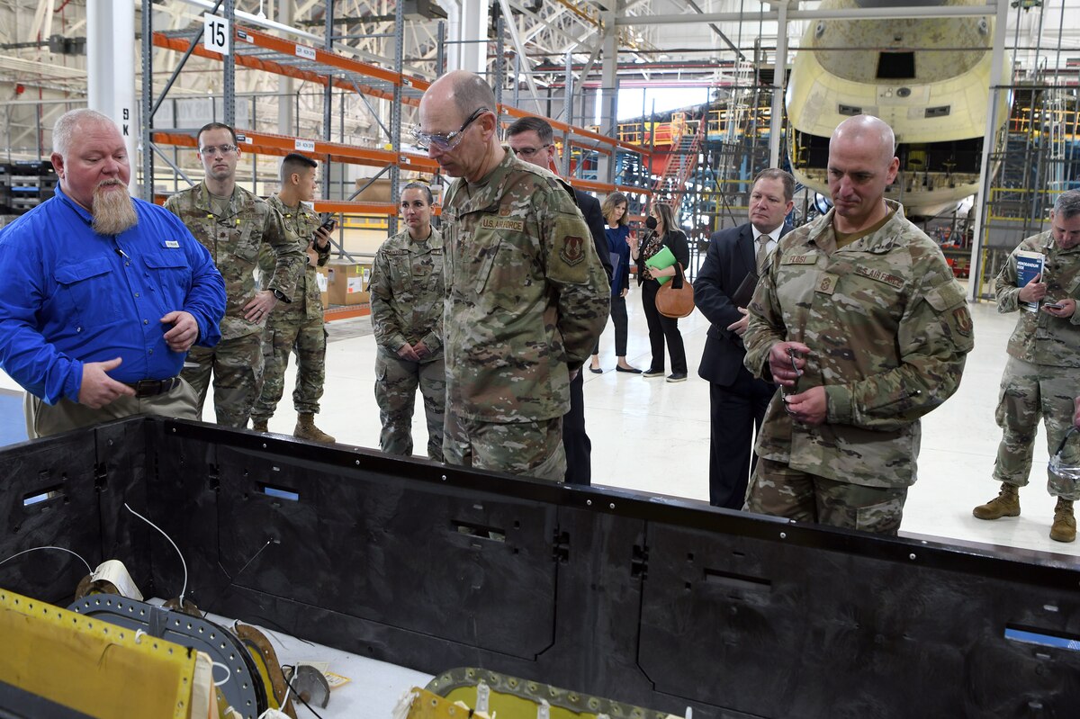 Photo shows group standing while looking at aircraft parts in a large box