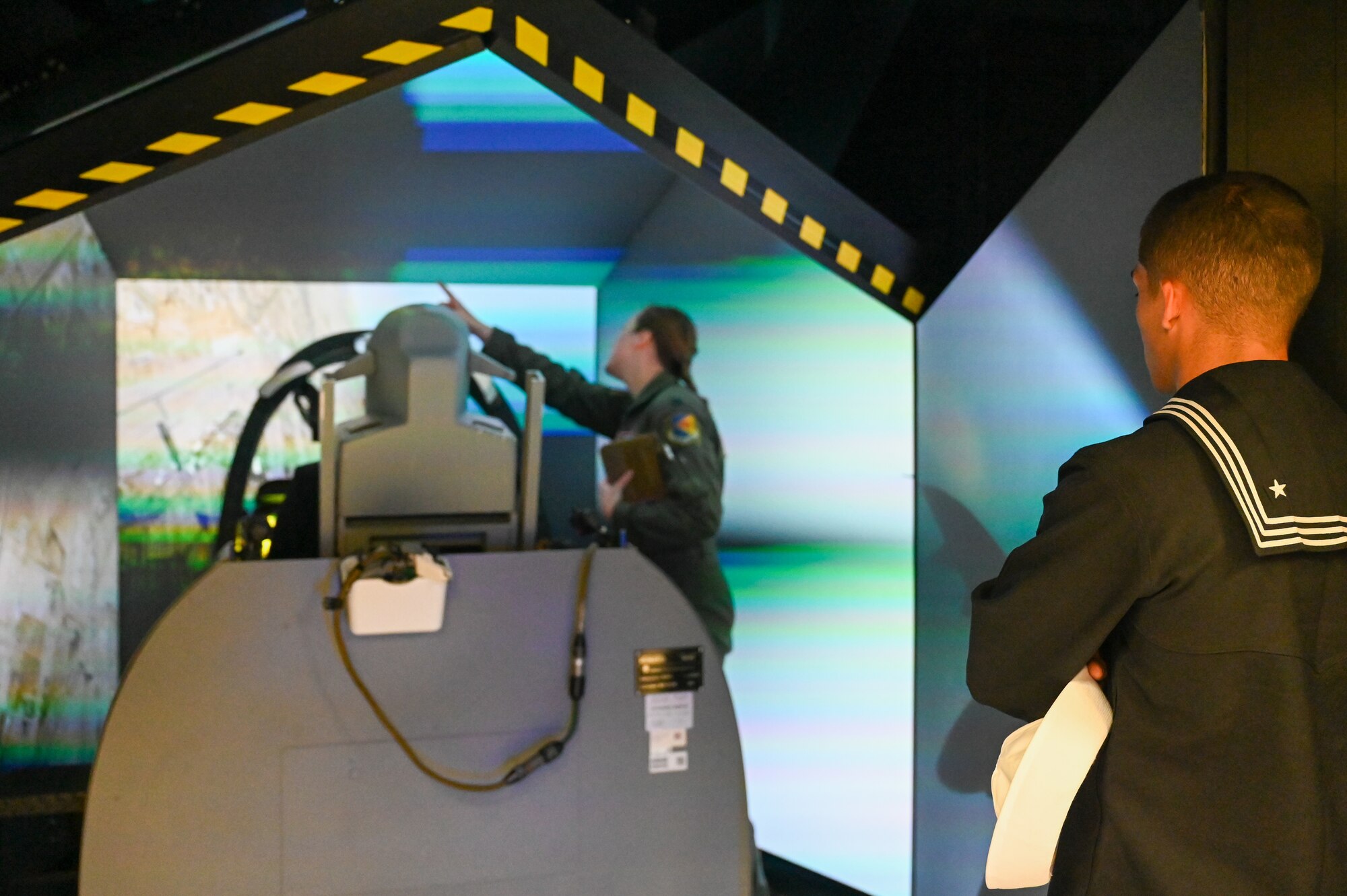 A photo of a Seaman watching while members are in an A-10 simulator.