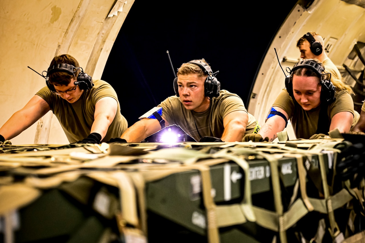 Airmen push a pallet of arms into the hold of an aircraft.