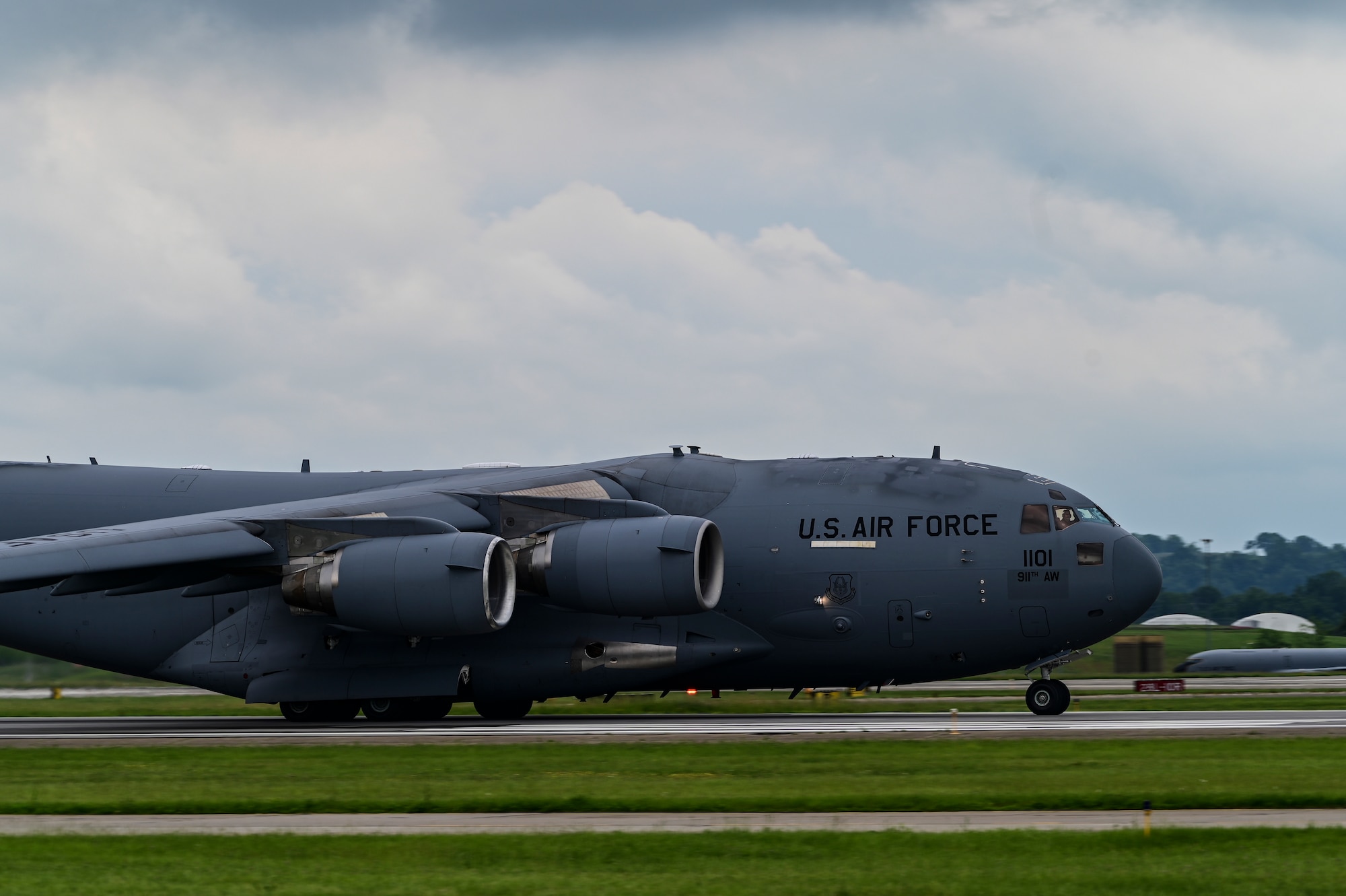 A C-17 aircraft accelerates for takeoff with a cloudy sky in the background
