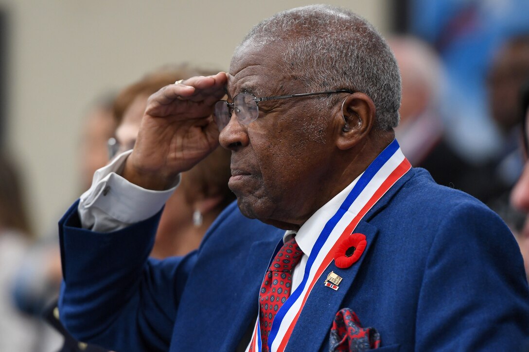 A veteran, shown in profile, salutes in a room.