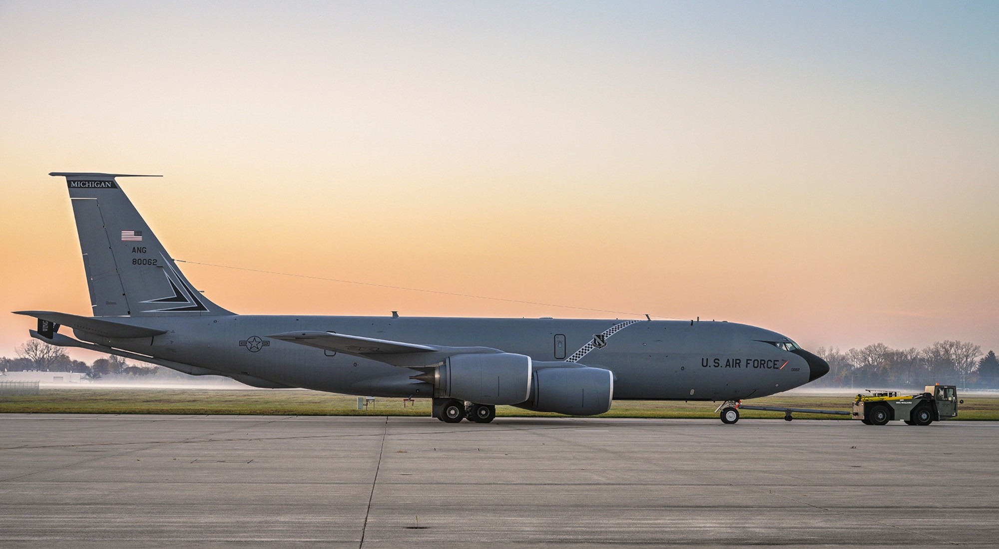 KC-135 towed by tow tractor down flightline, sunrise and fog in the background
