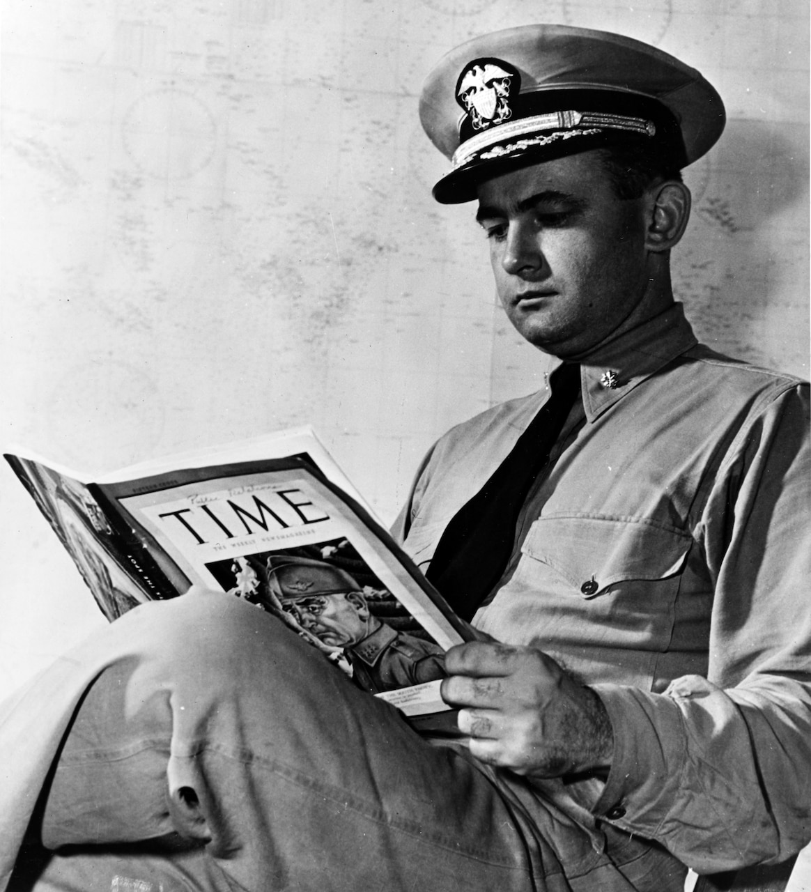 A seated man in uniform reads a copy of Time magazine.