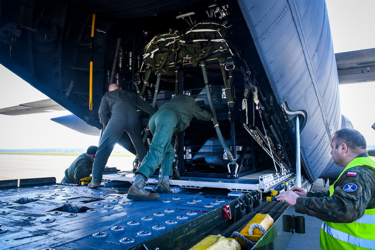 A Polish Air Force loadmaster, and personnel from U.S. Air Forces in Europe- Air Force Africa (USAFE-AF), and U.S. Special Operations Command Europe (SOCEUR), help guide the palletized precision effects cargo onto a Polish Air Force C-130 Hercules, Nov. 8, 2022, in Powidz, Poland. The Rapid Dragon Palletized Effects System, capable of deploying long-range cruise missiles using standard airdrop procedures from a cargo aircraft, was successfully deployed from an MC-130J Commando II on a Norwegian range Nov. 9, 2022.
