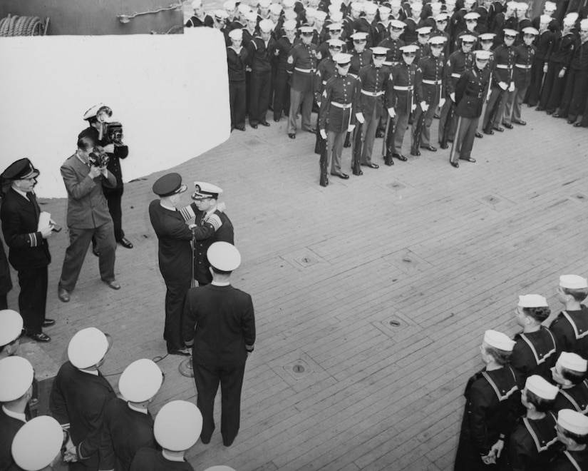 Several men stand around in formation as a man puts a medal around another man’s neck.