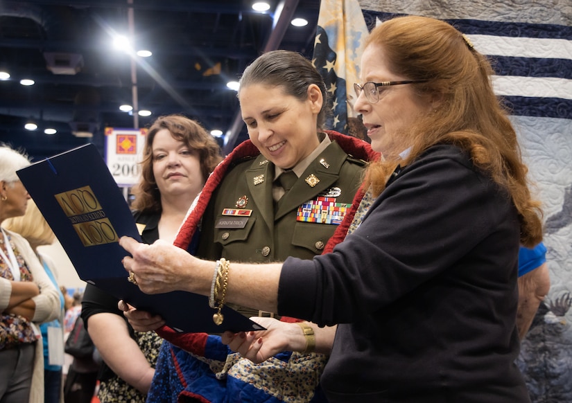 During opening day of the International Quilt Festival Nov. 3, 2022, in Houston, Donna Swanson (right), New Hampshire state coordinator, Quilts of Valor, reads a certificate of appreciation presented to Col. Tina L. Kirkpatrick (left), commander, 475th Quartermaster Group, U.S. Army Reserve. Kirkpatrick received a custom made quilt designed by Leo McClure, one of more than 10,000 Quilts of Valor members. Kirkpatrick, who also serves as the suicide prevention program manager for the 75th Innovation Command, plans to collaborate with Quilts of Valor, a national organization that has made more than 300,000 quilts designed specifically for veterans in honor of their service and sacrifice, to integrate quilting as a form of art therapy to enhance Soldier resiliency. (U.S. Army photo by Staff Sgt. John L. Carkeet IV, 75th Innovation Command).