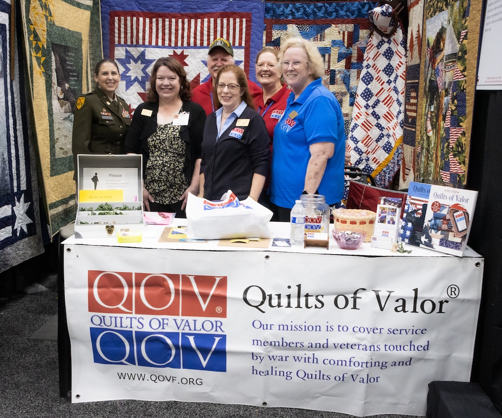 Col. Tina L. Kirkpatrick (left), commander, 475th Quartermaster Group, U.S. Army Reserve, stands with senior leaders and members of Quilts of Valor during the International Quilting Festival in Houston Nov. 3, 2022. Donna Swanson (third from left), New Hampshire state coordinator, Quilts of Valor, invited Kirkpatrick to the festival so she and her staff could present a custom quilt designed by Leo McClure, one of more than 10,000 Quilts of Valor members. Since 2003, the Quilts of Valor Foundation has covered veterans and service members touched by war with handmade quilts made by one of more than 10,000 Foundation members spread throughout the country. The Foundation achieved a major milestone when it produced its 300,000th quilt in April 2022. Kirkpatrick, who also serves as the suicide prevention program manager for the 75th Innovation Command, plans to collaborate with Quilts of Valor to integrate quilting as a form of art therapy to enhance Soldier resiliency. (U.S. Army photo by Staff Sgt. John L. Carkeet IV, 75th Innovation Command).