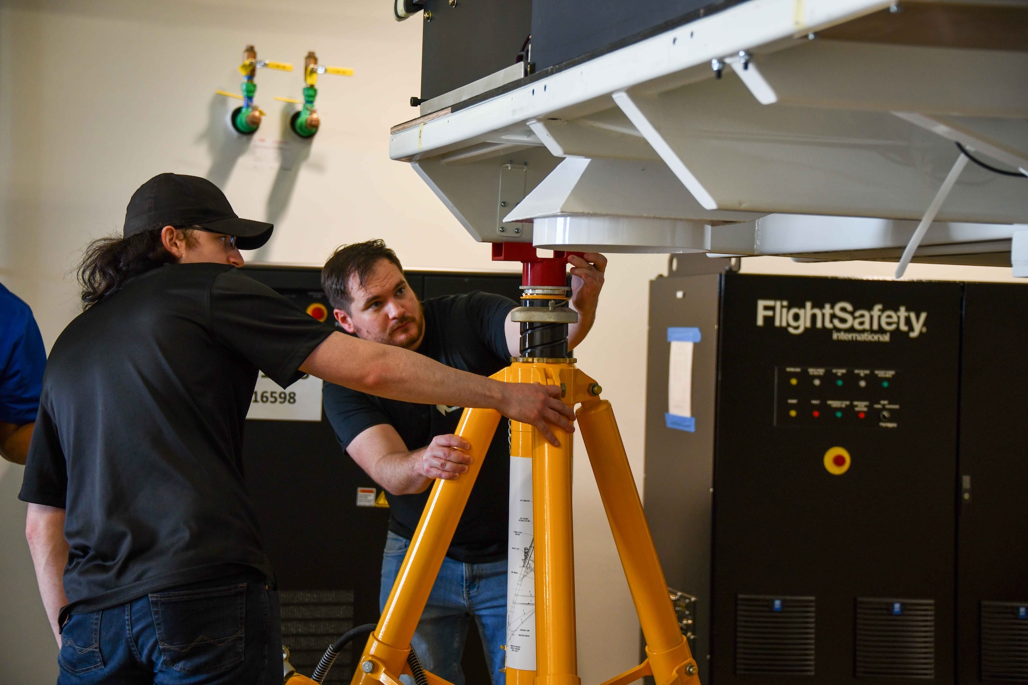 Two contractors adjust jacks under the KC-46 Pegasus boom operator simulator in the schoolhouse at Altus Air Force Base, Oklahoma, November 2, 2022. Though the newest simulators will be the last to arrive at AAFB for a while, leadership at the KC-46 school expects more as the schoolhouse takes on even more students in the years to come. (U.S. Air Force photo by Airman 1st Class Kari Degraffenreed)