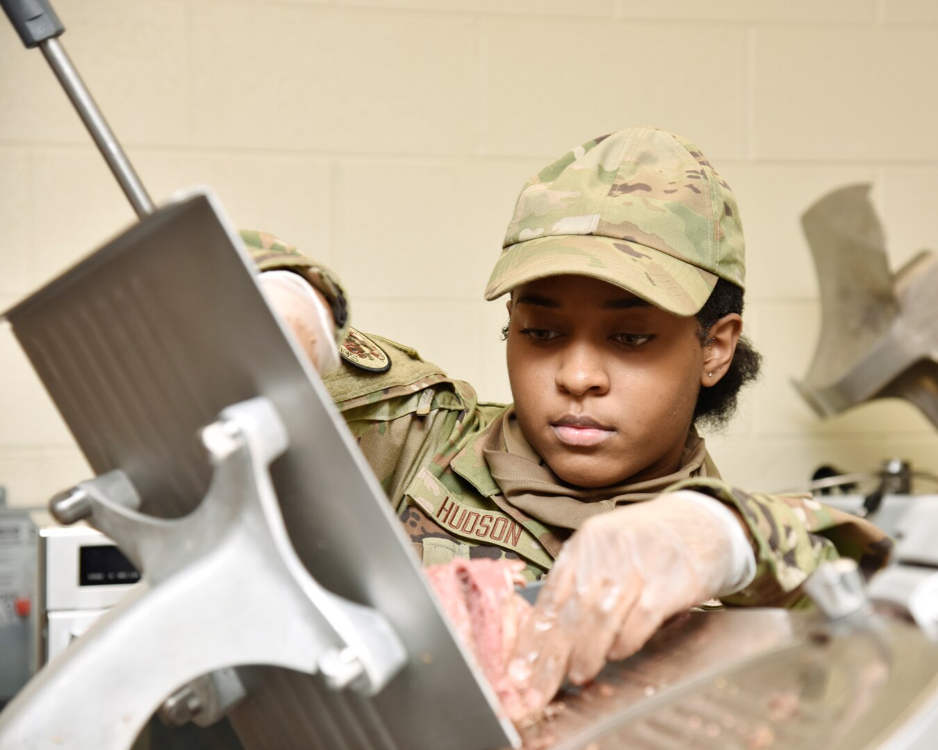 Female Airmen slices meat on industrial meat slicer.