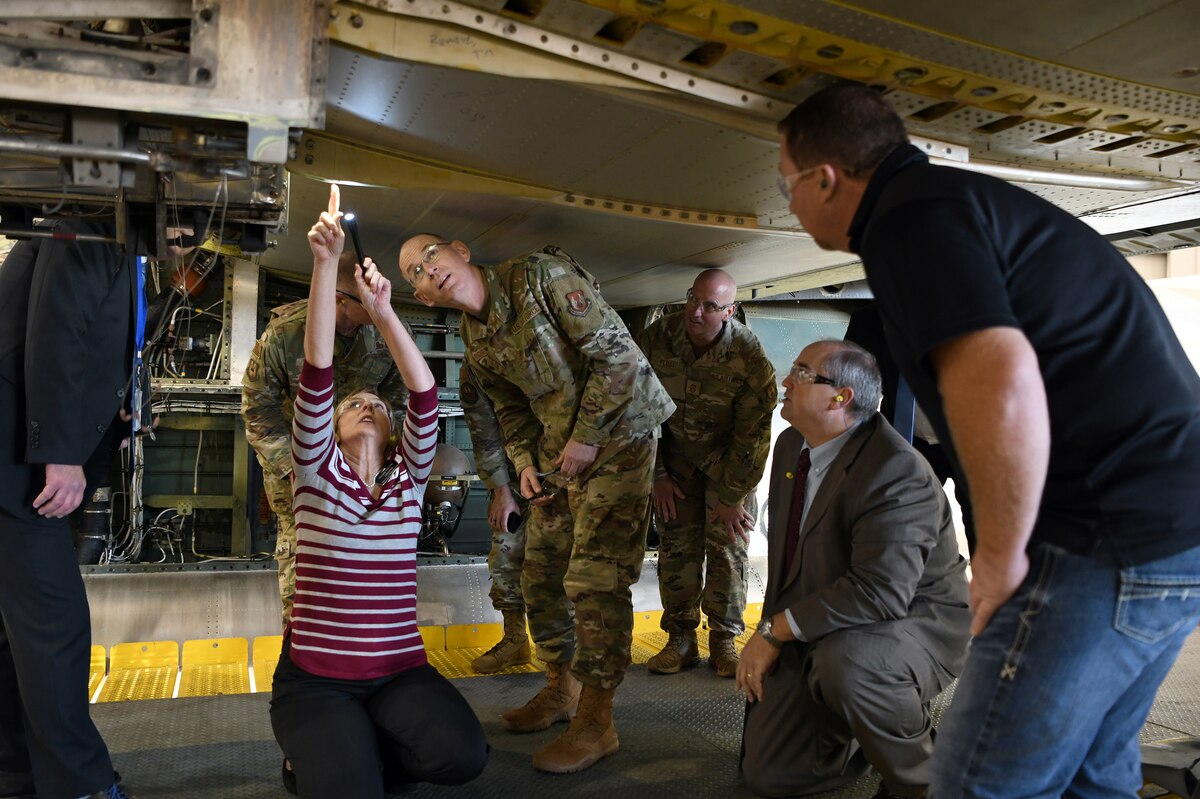 Photo shows people crouched under aircraft wing looking up at it with flashlight.