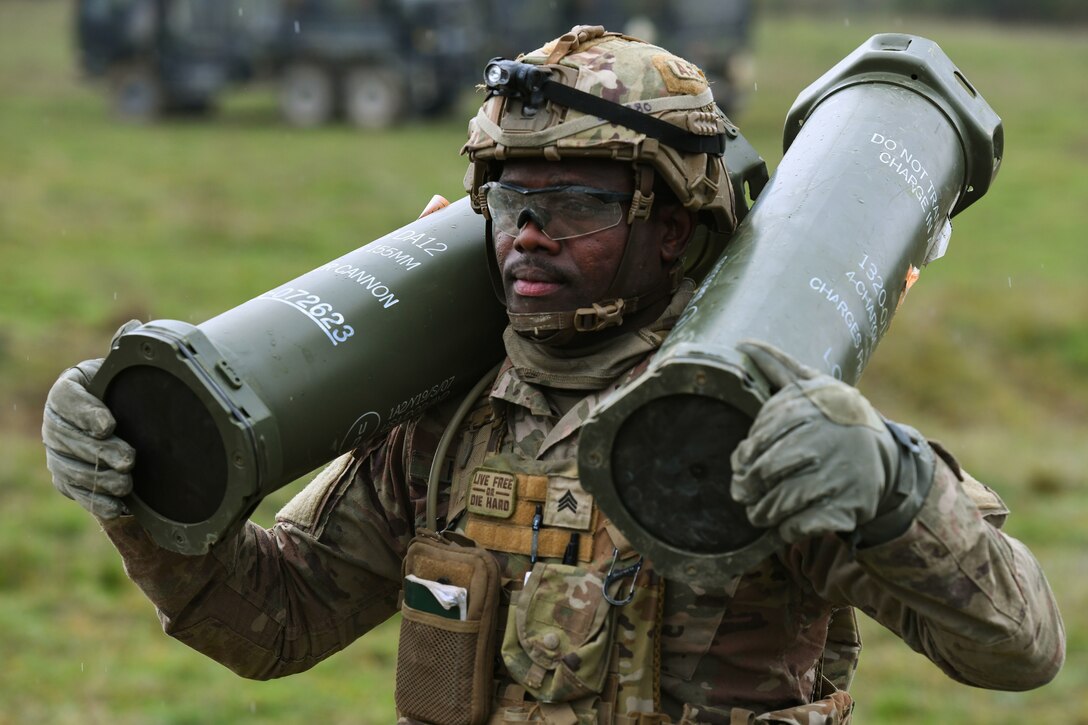 A soldier carries howitzer charges  on each shoulder.