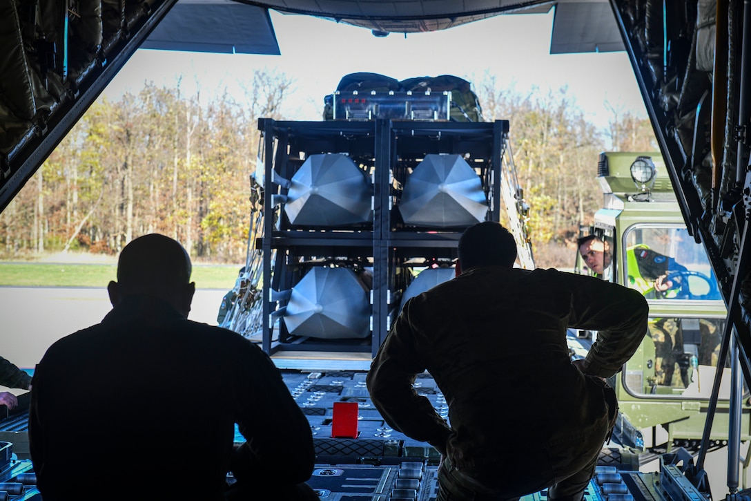 Airmen kneel in the back of an aircraft and look outwards at large weapons.