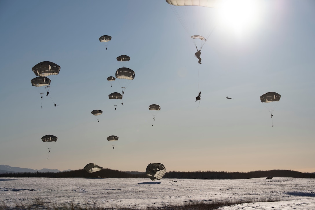 Paratroopers descend to a snow-covered field.