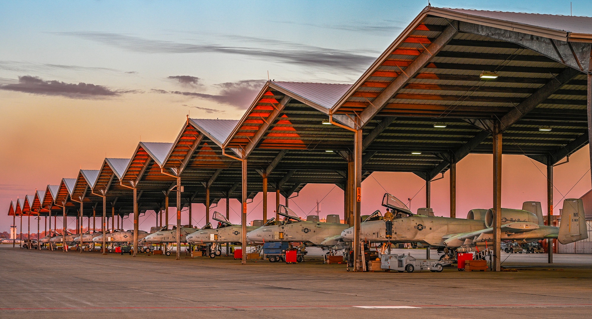 Eight A-10s parked in a line under sunshades. Last two and first three in line have canopies popped open with four maintainers at work.