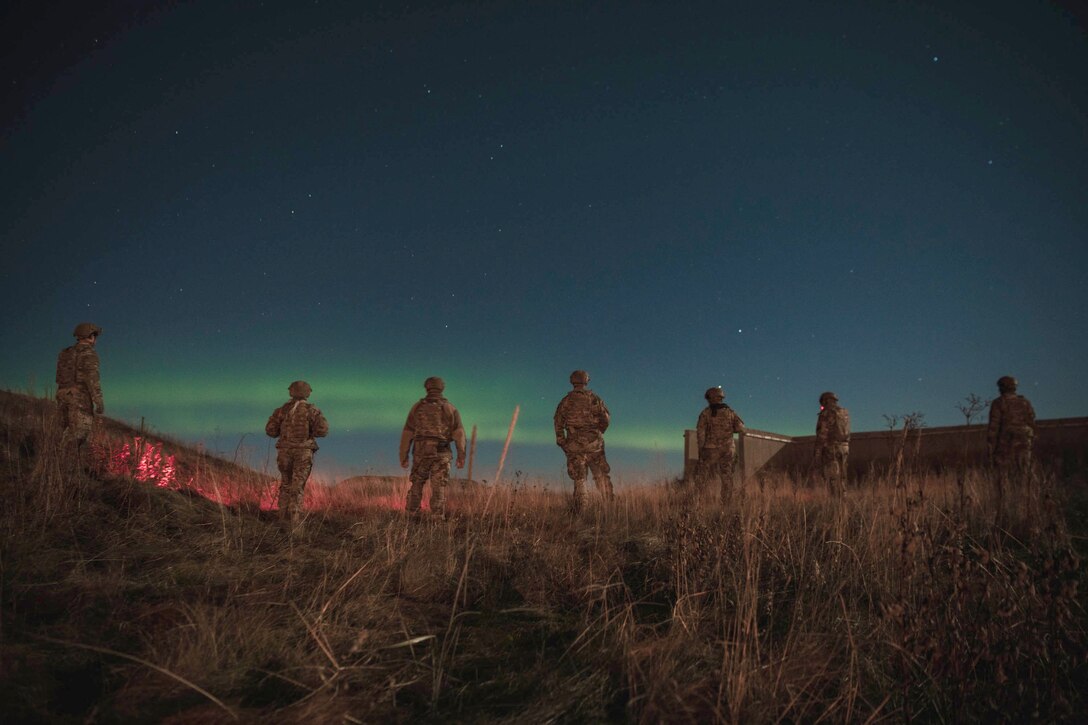 A group of airmen stand in a field under a starry sky.