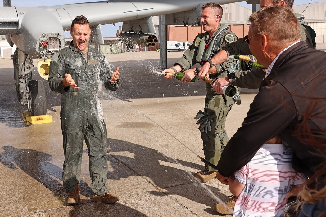 Pilot in jumpsuit is sprayed with water by fellow pilots and his children, parents.
