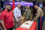 Man in uniform cuts the cake as others watch