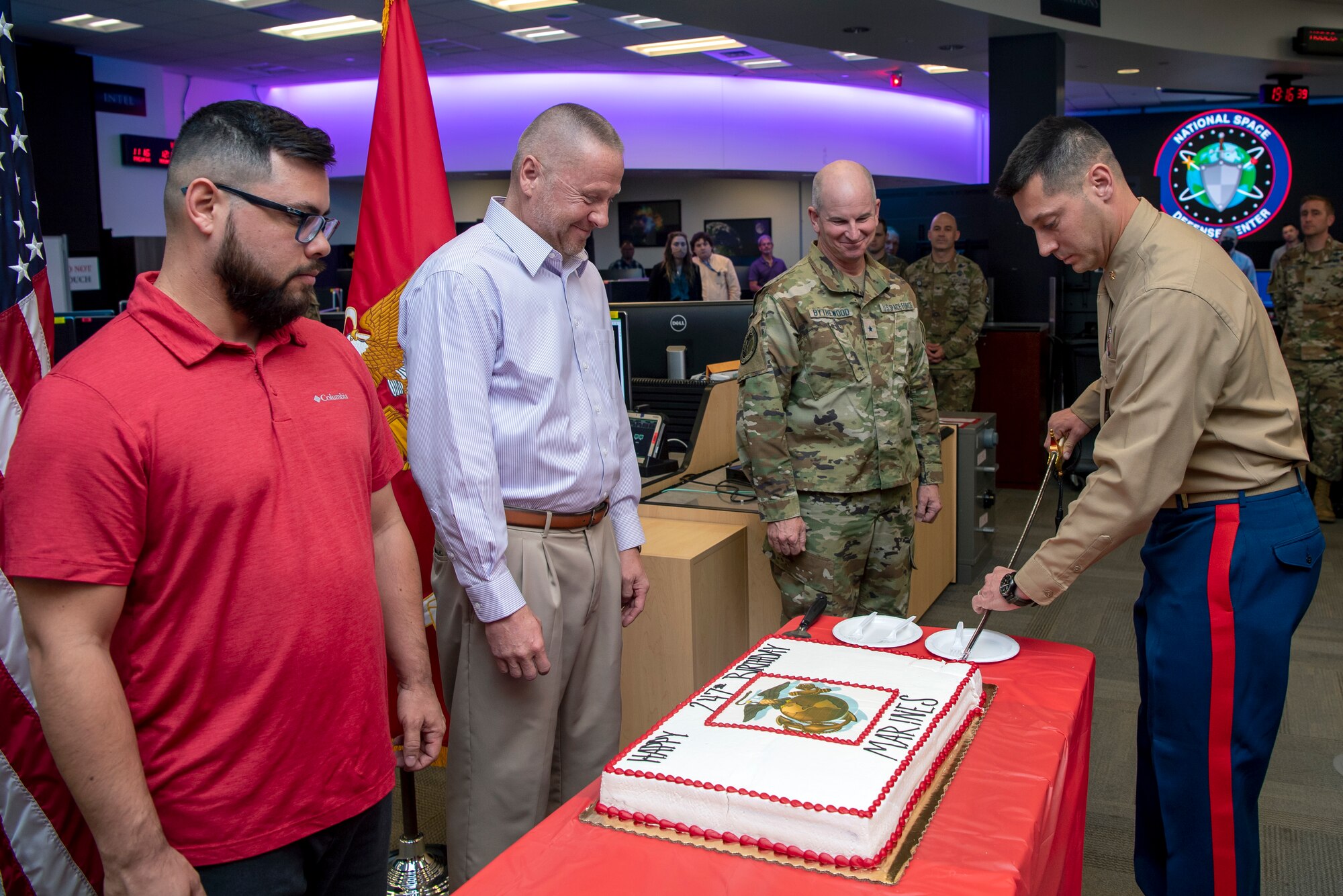 Man in uniform cuts the cake as others watch