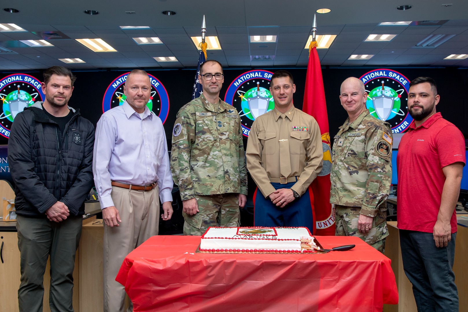 Military and civilians pose for a group photo in front of a sheet cake