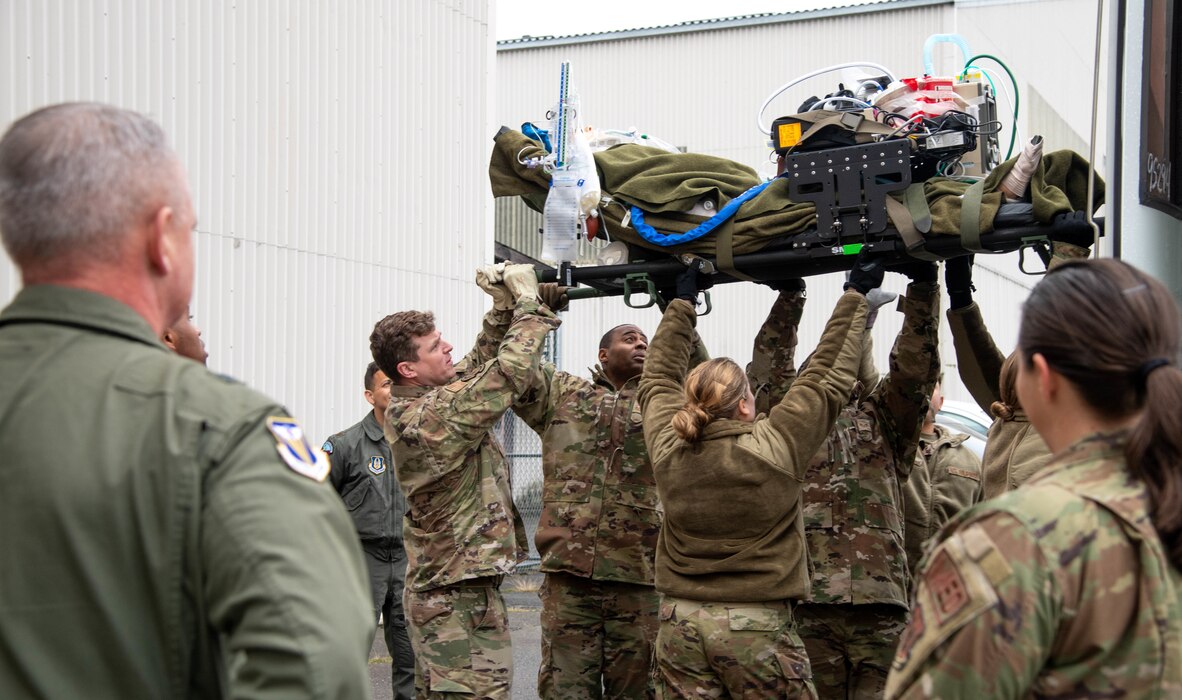 Airmen move a patient on a stretcher over their heads and onto a bus.