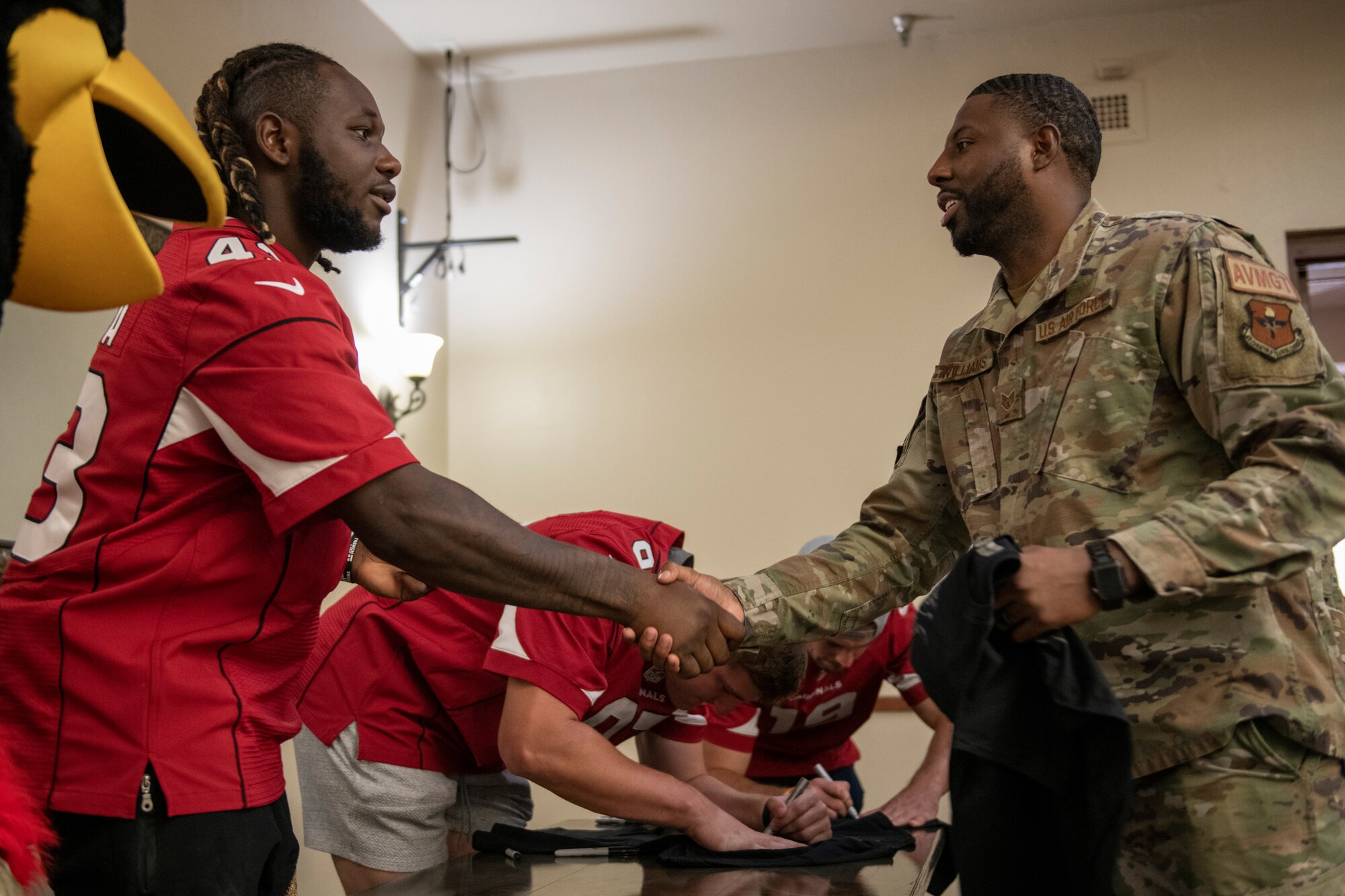 Jesse Luketa, Arizona Cardinals offensive linebacker, shakes hands with U.S. Air Force Staff Sgt. Jeffrey Williams, 63rd Fighter Squadron Aviation Resource Management noncommissioned officer in charge, after signing a t-shirt Nov. 1, 2022, at Luke Air Force Base, Arizona.