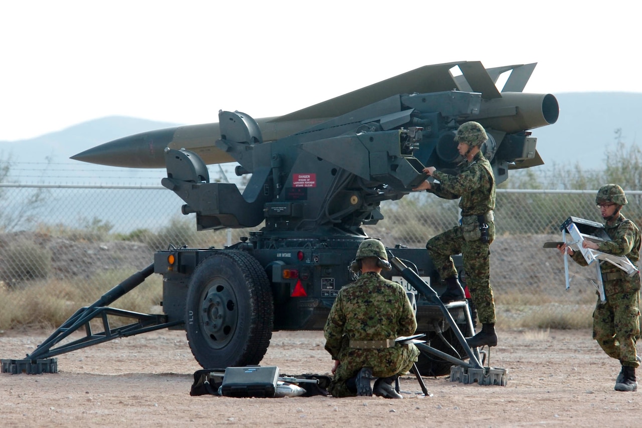Military personnel stand near a missile mounted on a launcher.
