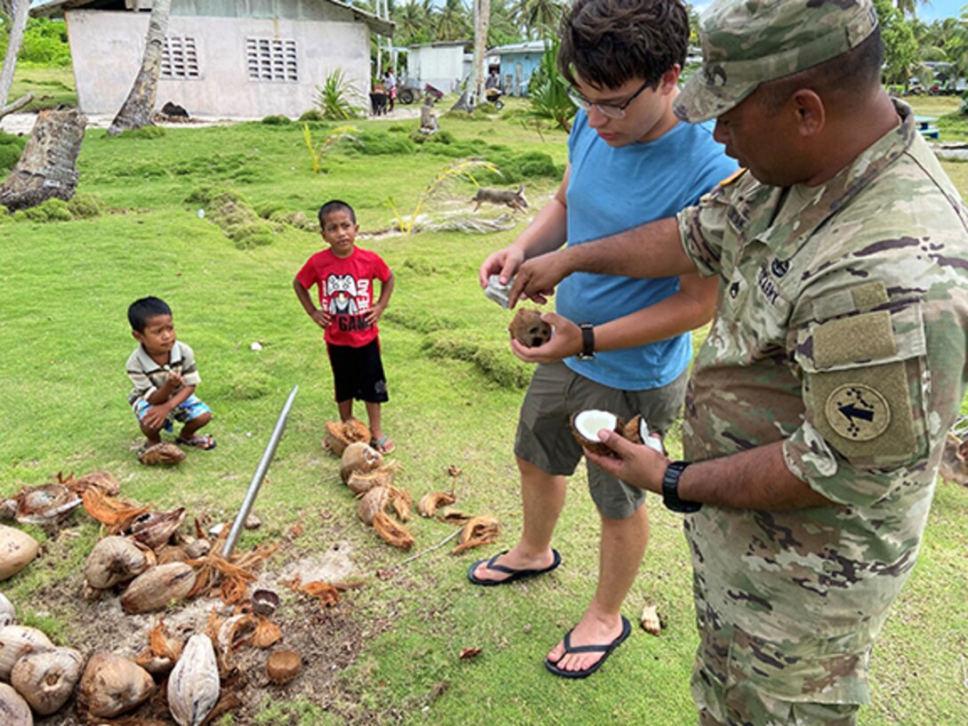Staff Sgt. Gary Likiak, right, a member of the two-man Oceania Engagement Team, explains proper coconut cracking techniques to Pacific Allies intern Simon Weiss.