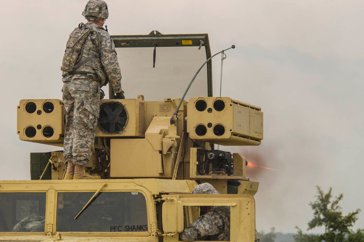 A soldier stands on a large piece of military hardware.