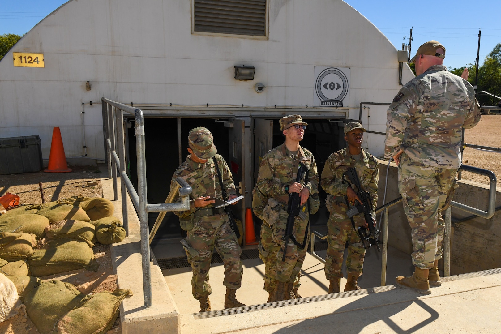 Three Airmen in uniform standing on stair steps facing another Airman while they are getting briefed