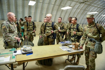 A group of Airmen standing around a table while listening to another Airman briefing them. They are all in military uniform.