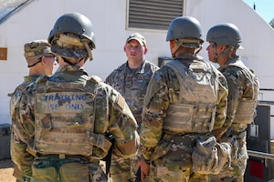 Five total Airmen in photo, with one facing toward the camera while he briefs the other four. They are all in military uniform.