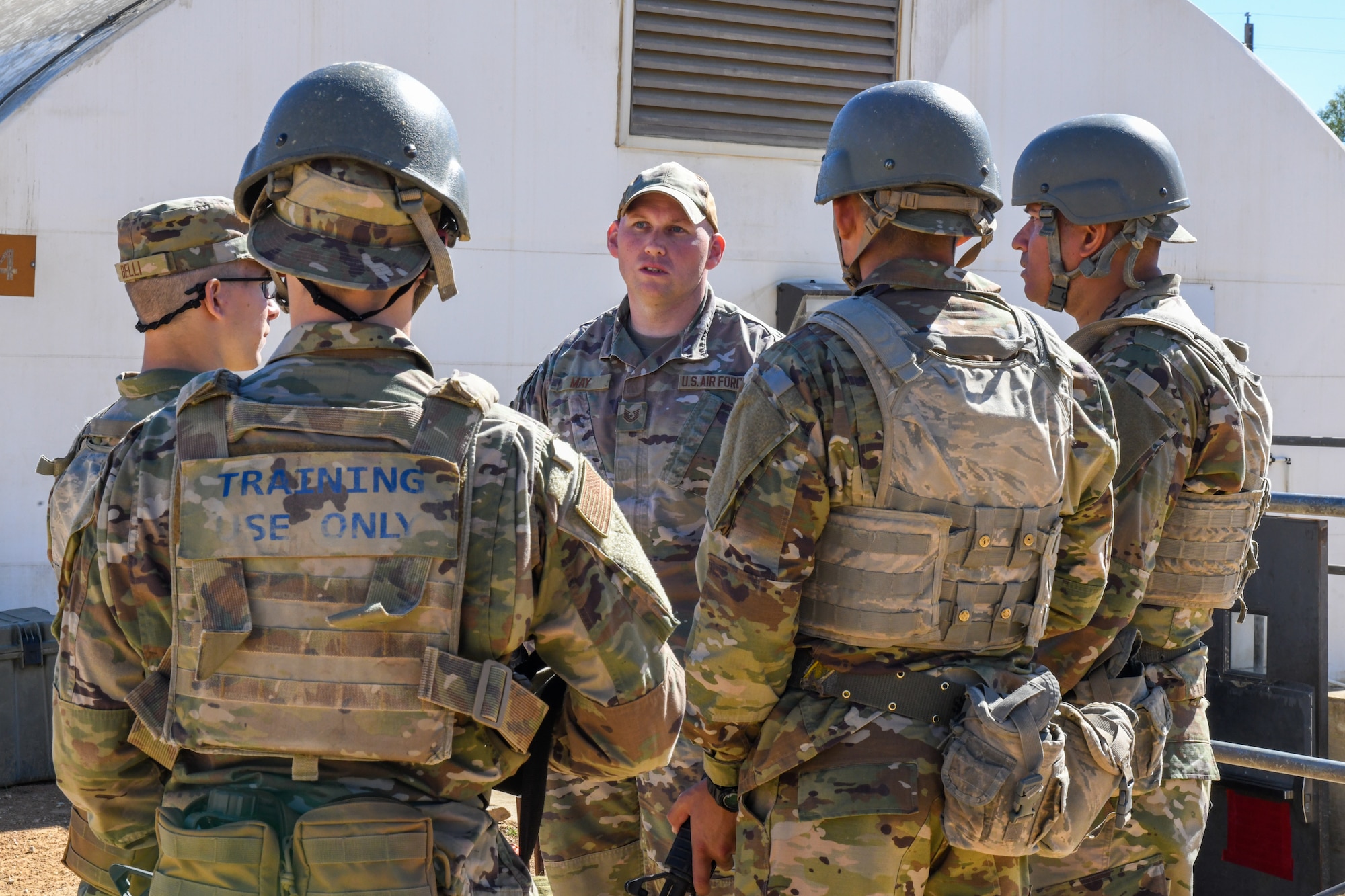 Five total Airmen in photo, with one facing toward the camera while he briefs the other four. They are all in military uniform.