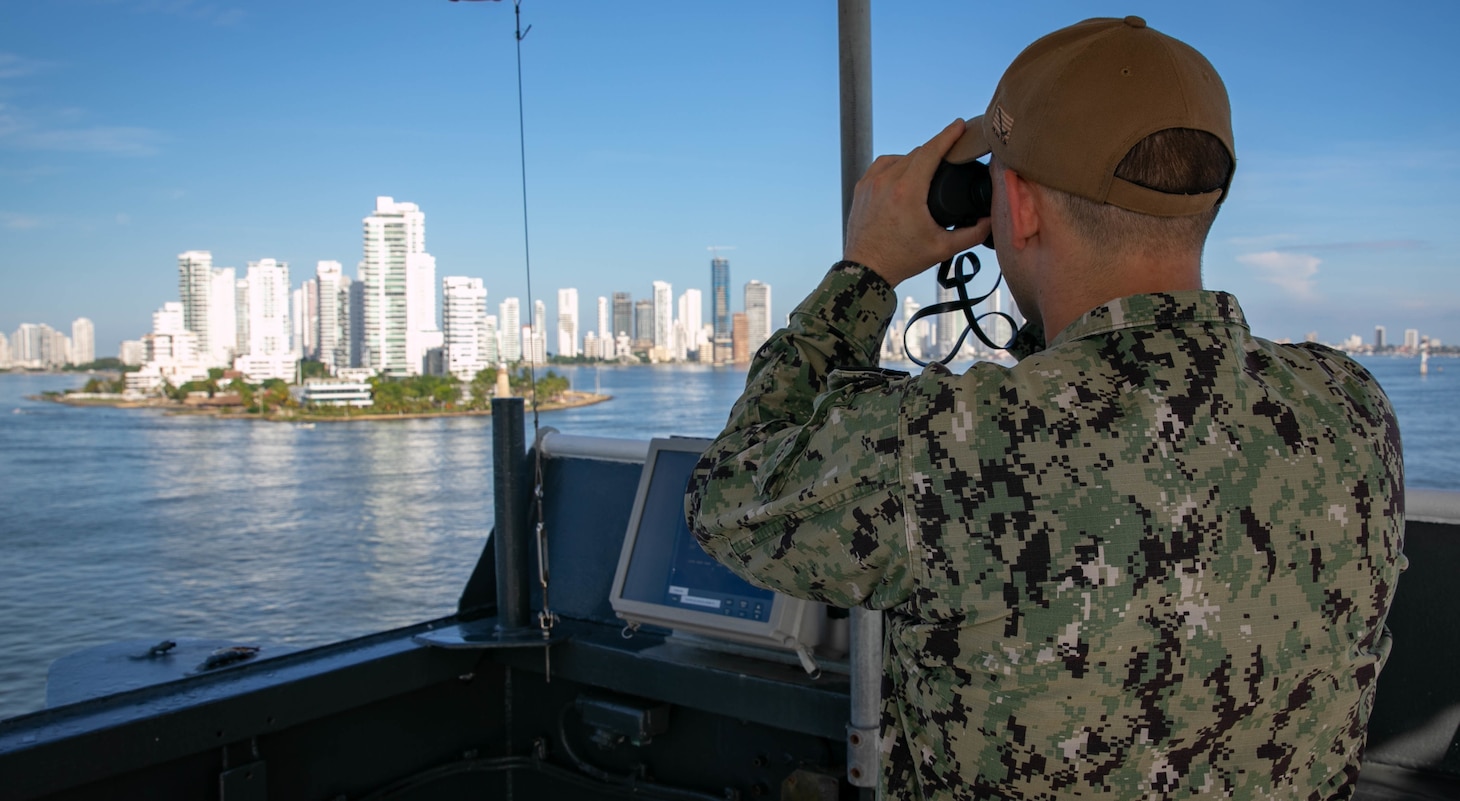 Master-at-Arms 1st Class Matthew Lowery, assigned to the hospital ship USNS Comfort (T-AH 20), looks at the skyline through binoculars during an inbound sea and anchor evolution as Comfort arrives in Cartagena, Colombia, Nov. 11, 2022.