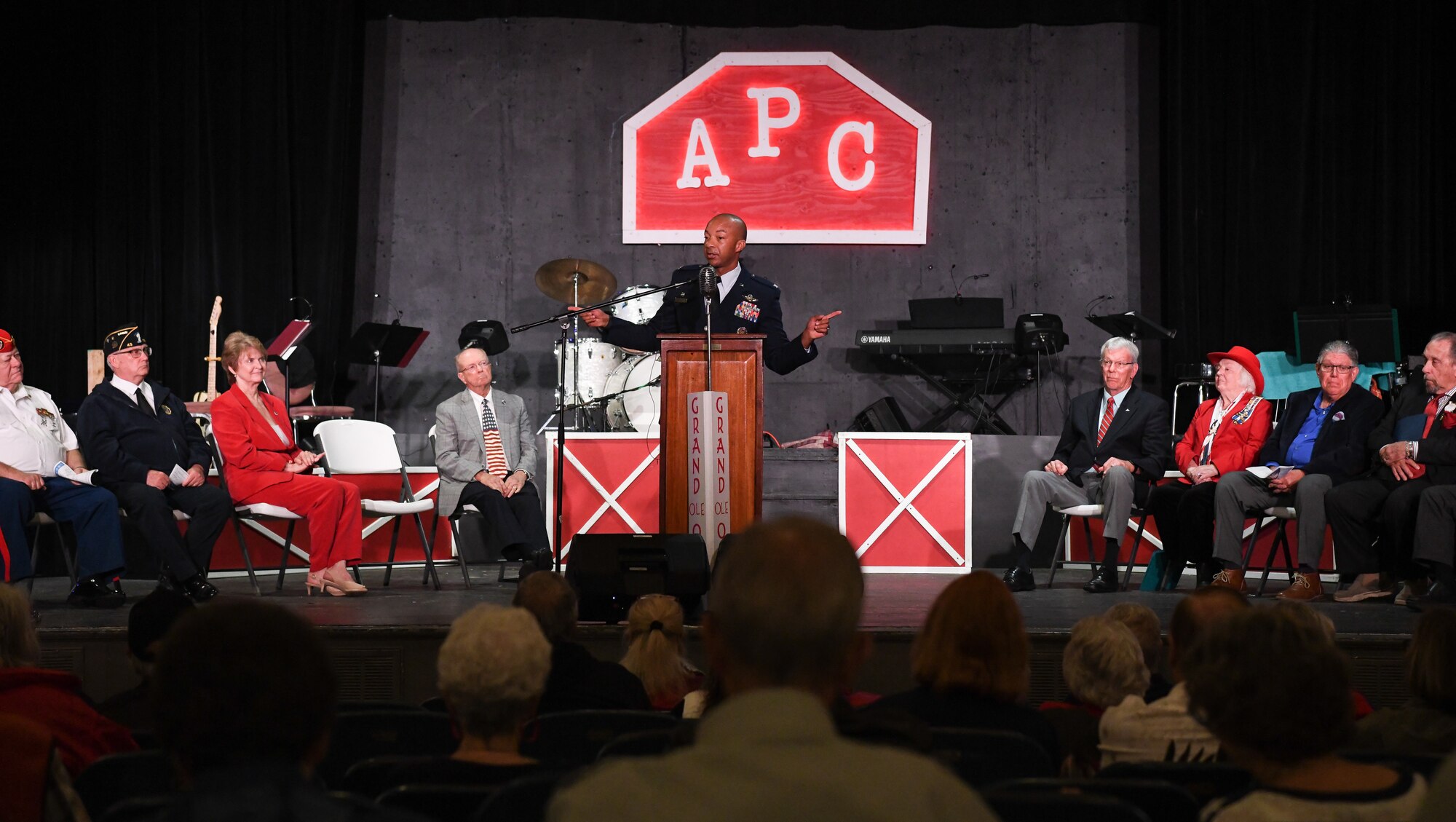 Col. Gordon speaking from lectern with others seated on stage