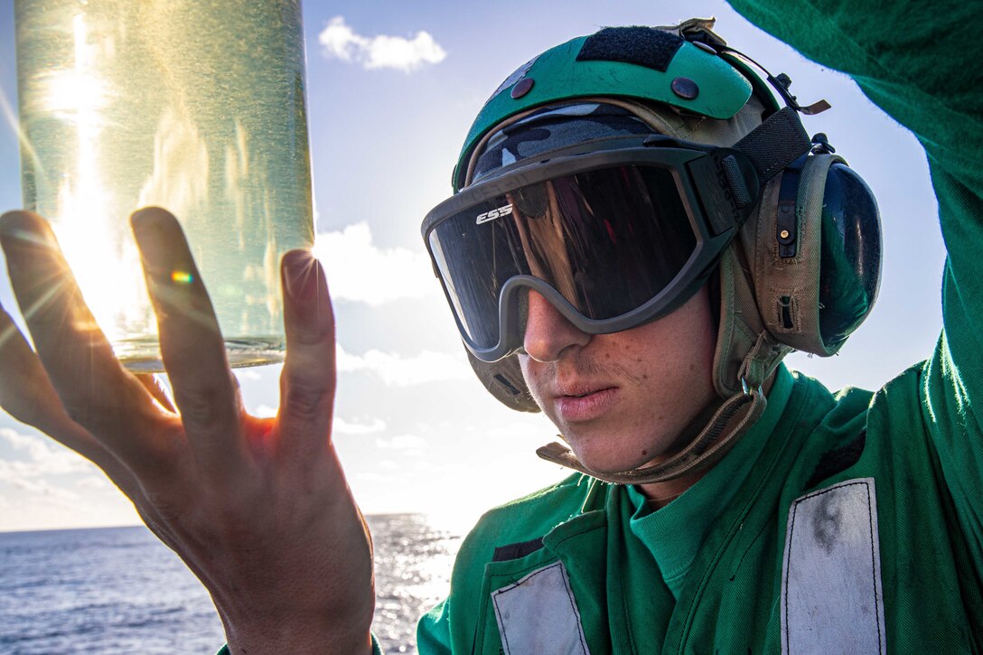 A sailor examines a large jar of fuel that he holds in his hand.