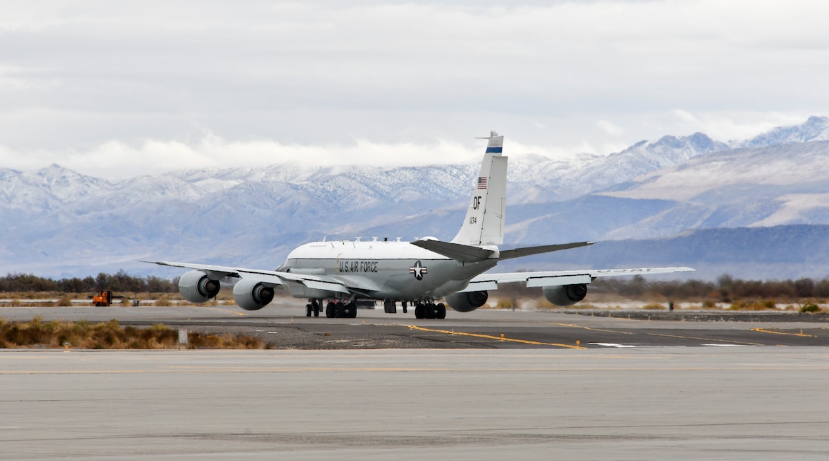 Airplane taxis on runway with snow-capped mountains in background