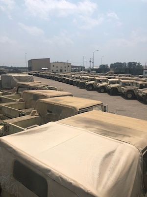 a large number of Humvees painted desert tan set in two lines outside.