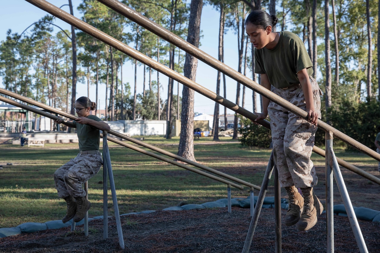 Two Marine Corps recruits balance with feet off the ground on an inclined beam obstacle.