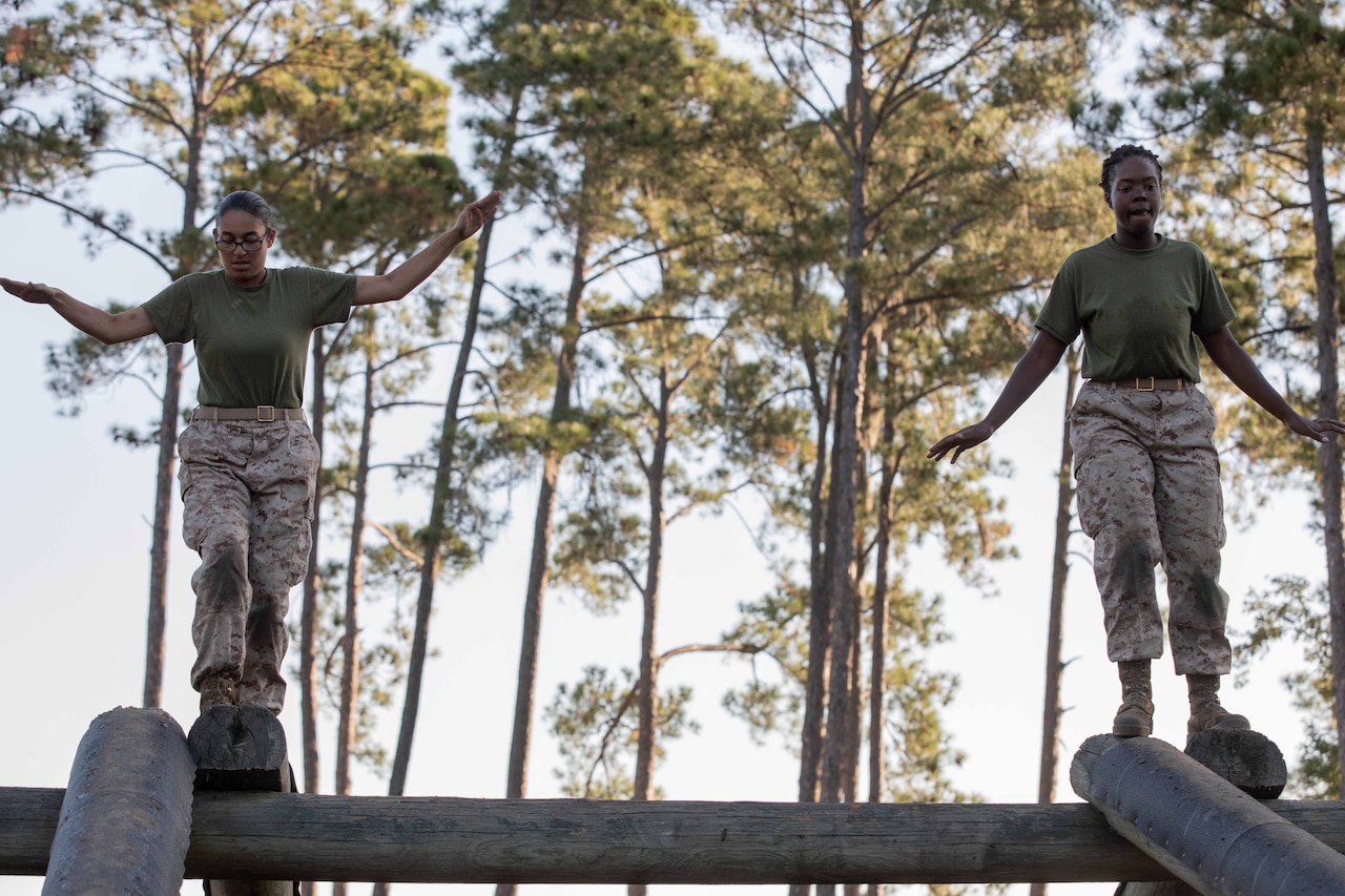 Two Marine Corps recruits balance with arms out while on an obstacle beam.