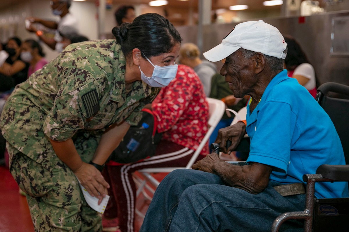 A sailor speaks with a patient in a gathering area aboard a ship.