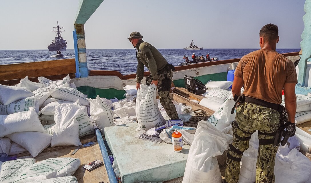 GULF OF OMAN (Nov. 9, 2022) Guided-missile destroyer USS The Sullivans (DDG 68) and patrol coastal ship USS Hurricane (PC 3) sail in the background as Sailors inventory a large quantity of urea fertilizer and ammonium perchlorate discovered on board a fishing vessel intercepted by U.S. naval forces while transiting international waters in the Gulf of Oman, Nov. 9.