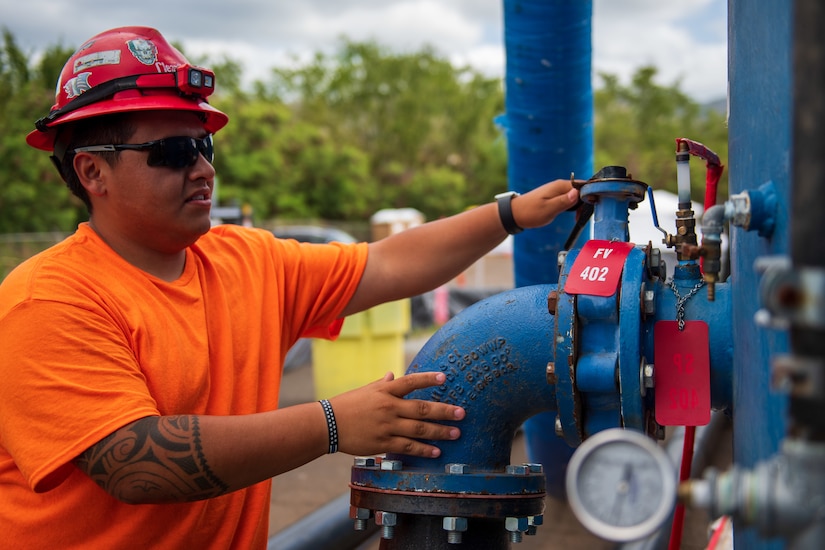 A man grips a valve handle on a large pipe.