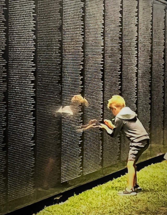 A child stencils a name from a panel of thousands displayed on the Wall That Heals, a three-quarter scale replica of the Vietnam Veterans Memorial in Washington, D.C., Oct. 28, 2022, in Anahuac, Texas.  At 350 feet long, and with its largest panel 7.5 feet high, this synthetic granite structure bears the names of the 58,281 men and women who made the ultimate sacrifice in Vietnam. More than 4,500 people visited the memorial while on display in Anahuac. The traveling exhibit will appear in 29 communities throughout the country this year. (Photo illustration courtesy of Wall That Heals - Chambers County)