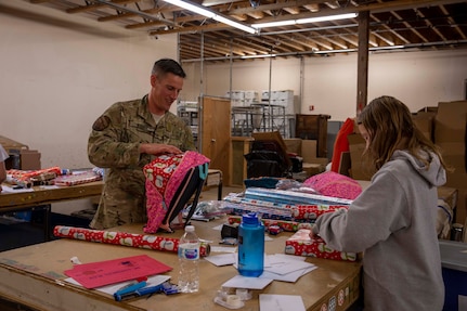 Air National Guard Lt. Col. Matthew Kirby, Alaska National Guard Joint Staff operations officer, wraps gifts with his daughter for Operation Santa Claus at the Salvation Army warehouse in Anchorage, Nov. 7, 2022. Operation Santa Claus is the AKNG’s yearly community relations and support program that provides gifts to children in remote communities across the state. In its 67th year, the program will celebrate with the communities of Scammon Bay, Minto and Nuiqsut. (Alaska National Guard photo by Victoria Granado)