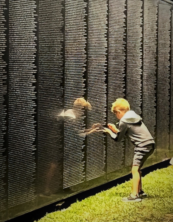 A child stencils a name from a panel of thousands displayed on the Wall That Heals, a three-quarter scale replica of the Vietnam Veterans Memorial in Washington, D.C., Oct. 28, 2022, in Anahuac, Texas.  At 350 feet long, and with its largest panel 7.5 feet high, this synthetic granite structure bears the names of the 58,281 men and women who made the ultimate sacrifice in Vietnam. More than 4,500 people visited the memorial while on display in Anahuac. The traveling exhibit will appear in 29 communities throughout the country this year. (Photo illustration courtesy of Wall That Heals - Chambers County)