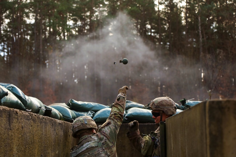 One soldier throws a hand grenade while another looks on during readiness training.