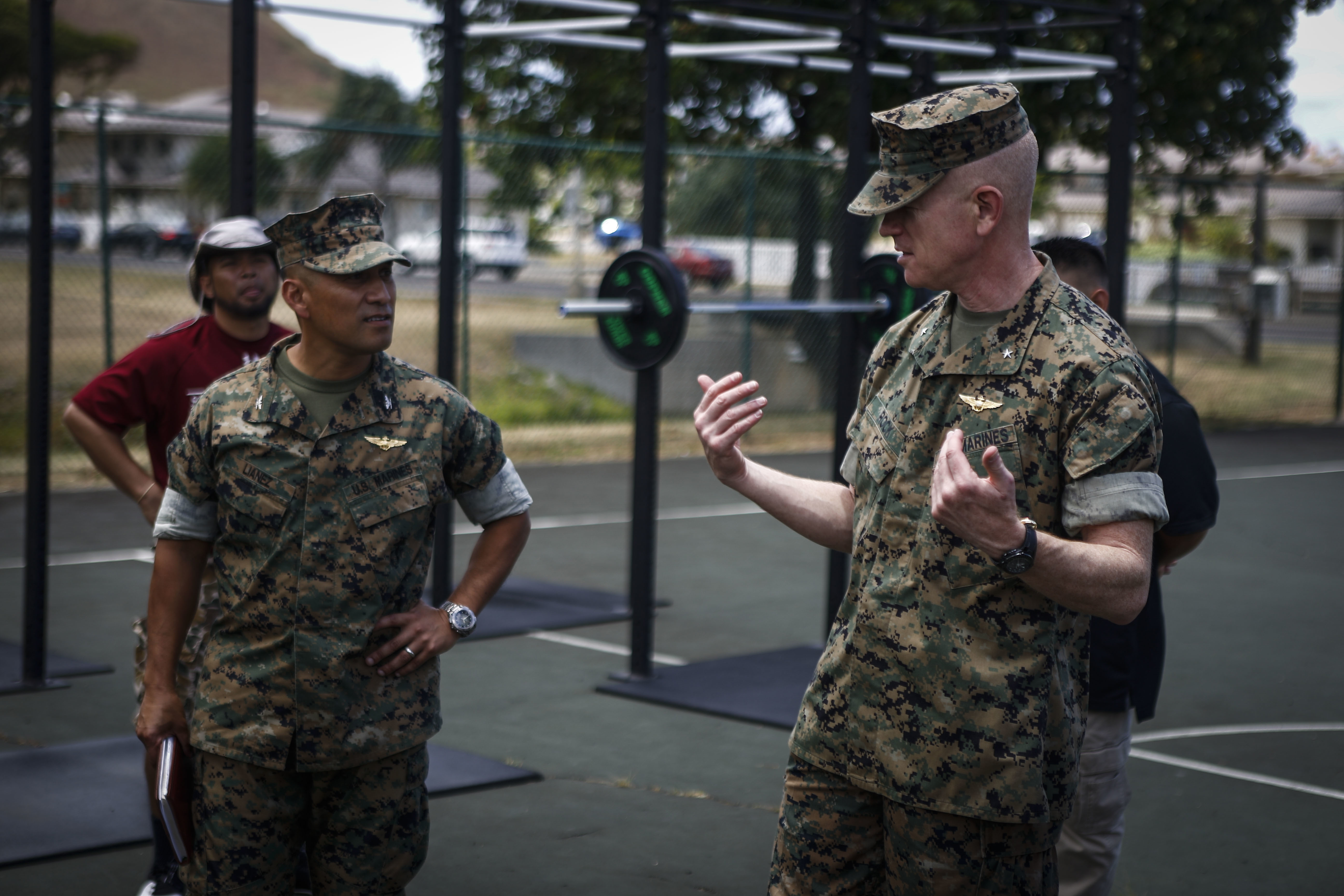 Two Marines in uniform, speaking to each other in an outdoor gym.